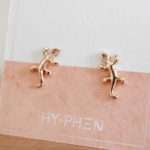 Op de afbeelding: Een paar gouden hagedis oorbel studs. De oorbellen zijn klein en delicaat, en ze hebben een eenvoudig, minimalistisch ontwerp.