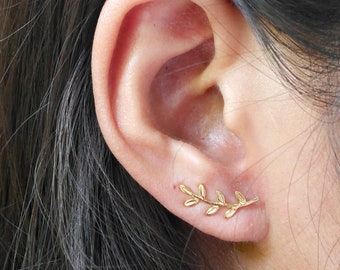 May include: Gold leaf ear climber earrings. The earrings are shaped like a branch with small leaves. The earrings are worn in the upper part of the ear.