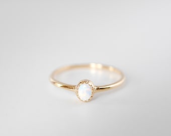May include: A delicate gold ring with a white opal gemstone set in a scalloped bezel.