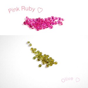 Puede incluir: Gemas de rub&iacute; rosa y oliva. Un mont&oacute;n de gemas de rub&iacute; rosa y una dispersi&oacute;n de gemas de color verde oliva sobre un fondo blanco.