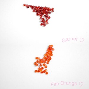 Puede incluir: Dos montones de piedras preciosas rojas sobre una superficie blanca. El mont&oacute;n superior est&aacute; etiquetado como "Granate" y el mont&oacute;n inferior est&aacute; etiquetado como "Naranja Fuego".