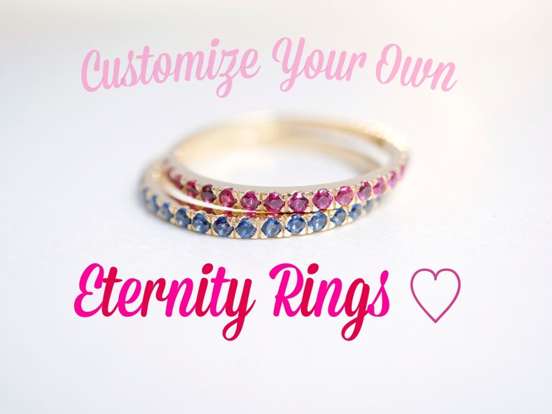 Puede incluir: Dos anillos de eternidad de oro con una fila de peque&ntilde;as piedras preciosas azules y rojas. Los anillos est&aacute;n apilados uno encima del otro. El texto "Customize Your Own Eternity Rings" est&aacute; escrito en rosa sobre los anillos. Un coraz&oacute;n rosa est&aacute; debajo del texto.