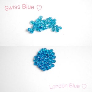 Puede incluir: Dos montones de peque&ntilde;as piedras preciosas redondas azules. El mont&oacute;n de arriba est&aacute; etiquetado como "Swiss Blue" y el mont&oacute;n de abajo est&aacute; etiquetado como "London Blue".