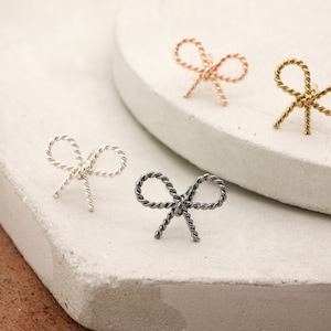 May include: Four small bow-shaped earrings in silver, gold, rose gold, and black.