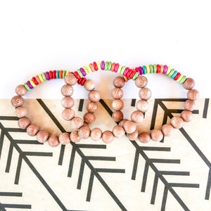 May include: Three wooden bead bracelets with colorful accents. The bracelets are stacked on top of each other and have a natural wood finish.
