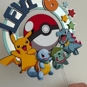 Pu&ograve; includere: Un topper per torta con una Pok&eacute; Ball, Pikachu, Squirtle e Bulbasaur. Il topper &egrave; decorato con stelle e il nome "Levi" e il numero "6".