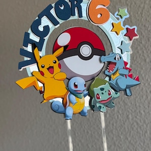 Pu&ograve; includere: Un topper per torta con una Pok&eacute; Ball blu, rossa e bianca con un Pikachu giallo, uno Squirtle blu e un Bulbasaur verde. Il topper include anche il nome "Victor" e il numero "6" in un cerchio blu con stelle arancioni.