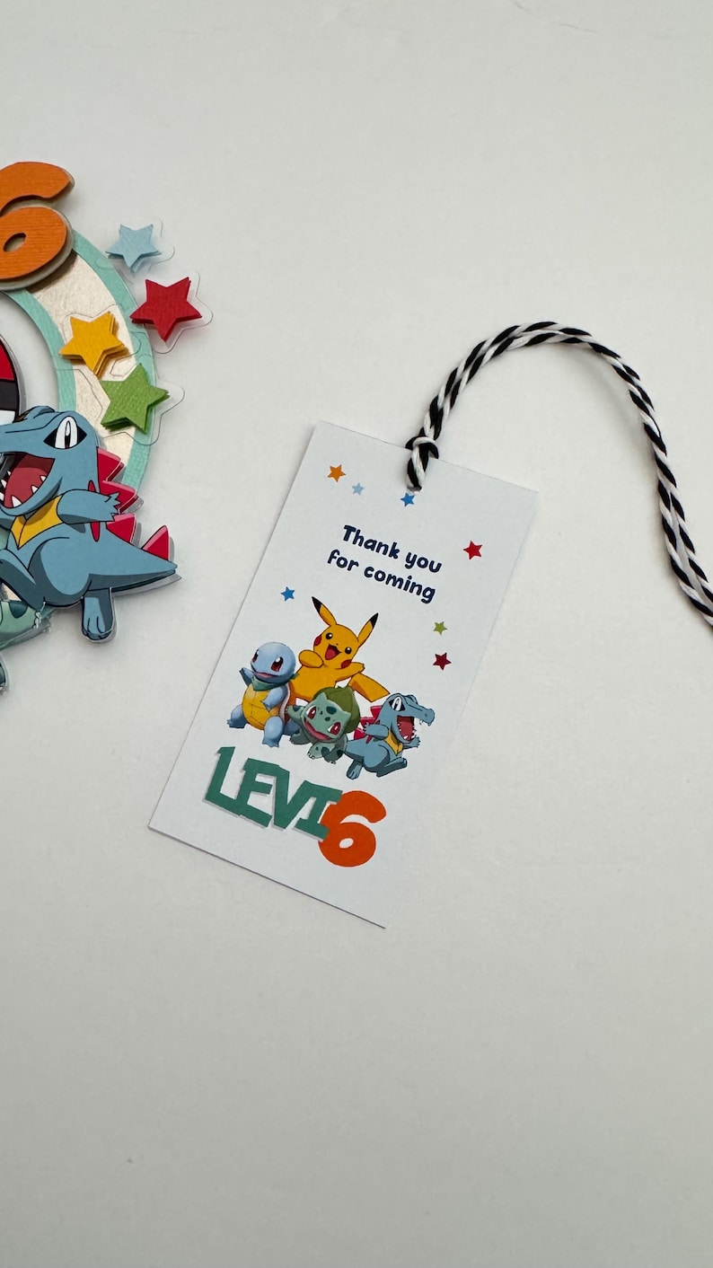Pu&ograve; includere: Un'etichetta di ringraziamento bianca con un'immagine di personaggi Pokemon in cartone animato colorato. L'etichetta dice "Grazie per essere venuto" e "Livello 6".