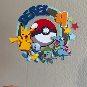 Pu&ograve; includere: Un topper per torta con il nome "Derek" in lettere blu, un numero "4" in arancione, una Pok&eacute; Ball, Pikachu, Squirtle, Bulbasaur e Charmander. Il topper &egrave; su un bastoncino di plastica trasparente.
