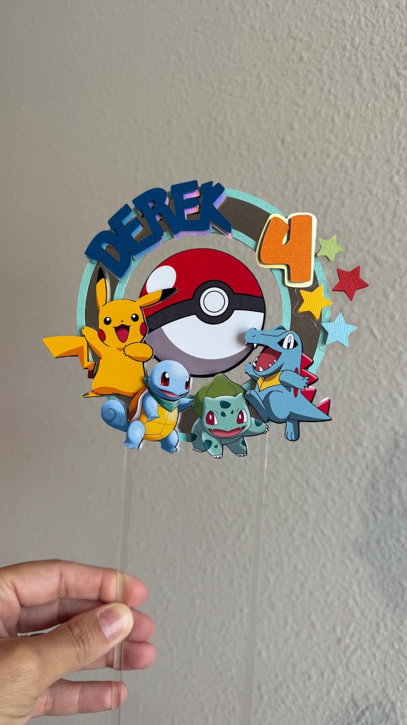 Pu&ograve; includere: Un topper per torta con il nome "Derek" in lettere blu, un numero "4" in arancione, una Pok&eacute; Ball, Pikachu, Squirtle, Bulbasaur e Charmander. Il topper &egrave; su un bastoncino di plastica trasparente.