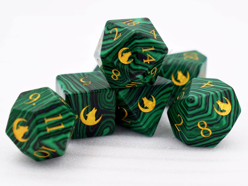 Puede incluir: Un conjunto de siete dados poli&eacute;dricos verdes y negros, con n&uacute;meros dorados y un s&iacute;mbolo de lobo y luna creciente. Los dados, con efecto veteado, se muestran sobre un fondo blanco, ideales para juegos de mesa.