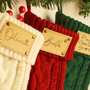 Può includere: Tre calze di Natale a treccia color crema, rosse e verdi. Ogni calza ha un'etichetta in legno con i nomi: Olivia, Bella e Charlotte. Decorazioni natalizie festive.
