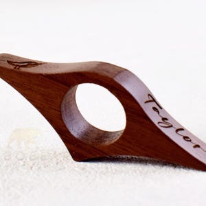 May include: A wooden book page holder with a curved design. The holder is engraved with the name "Taylor" and a small bird design.