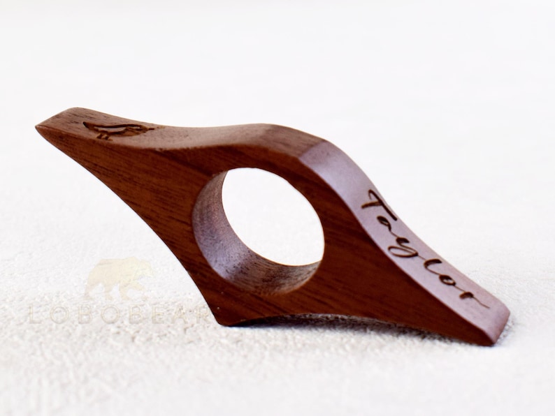 May include: A wooden book page holder with a curved design. The holder is engraved with the name "Taylor" and a small bird design.