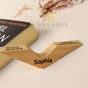 Peut inclure: Un support de livre en bois avec les mots "Book Whore", "Spread Those Pages" et "Sophia" grav&eacute;s dessus. Le support est brun clair et a une forme de V.
