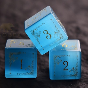 Peut inclure: Trois d&eacute;s bleus translucides avec des chiffres dor&eacute;s et des filigranes d&eacute;coratifs. Les d&eacute;s sont dispos&eacute;s de mani&egrave;re dynamique, avec un d&eacute; inclin&eacute;. Les chiffres 1, 2, 3 et 6 sont visibles. D&eacute;s pour jeux de soci&eacute;t&eacute;.