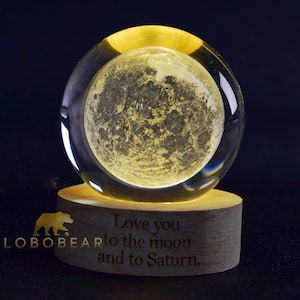 Puede incluir: Una esfera de vidrio con una imagen detallada de la luna en su interior, sentada sobre una base de madera con la inscripción "Love you to the moon and to Saturn."