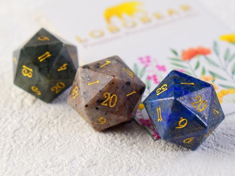 May include: Three 20-sided dice made of natural stone. The dice are green, brown, and blue with gold numbers.
