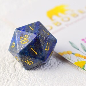 May include: A blue and gold gemstone d20 dice with gold numbers. The dice is made of lapis lazuli.