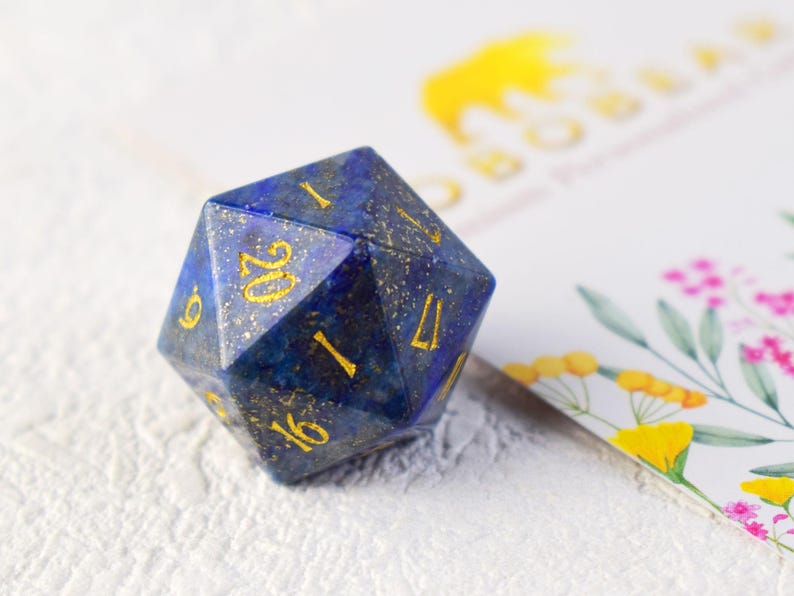 May include: A blue and gold gemstone d20 dice with gold numbers. The dice is made of lapis lazuli.