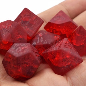 May include: A set of seven red polyhedral dice with a Celtic knot design. The dice are translucent and have a frosted finish.