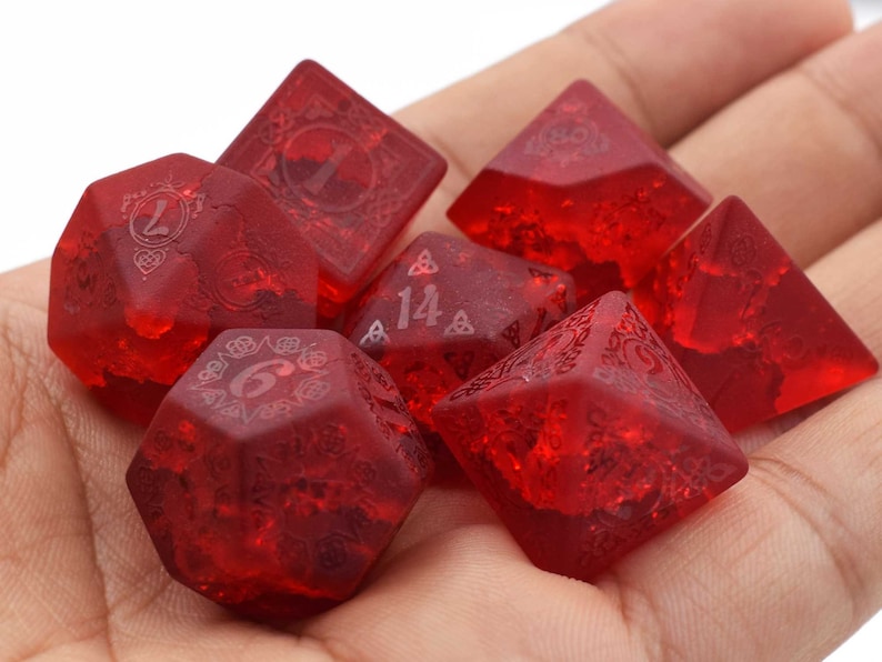 May include: A set of seven red polyhedral dice with a Celtic knot design. The dice are translucent and have a frosted finish.