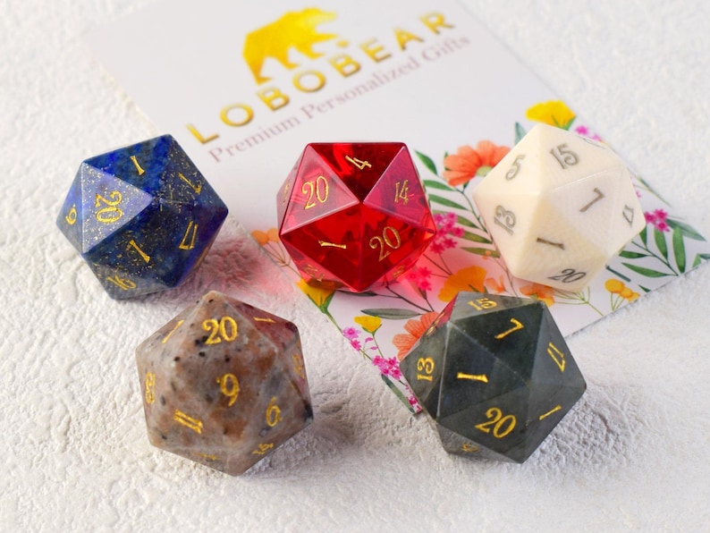 May include: Five 20-sided dice made from different materials. The dice are in various colours, including blue, red, white, brown, and green. The dice are all marked with gold numbers.