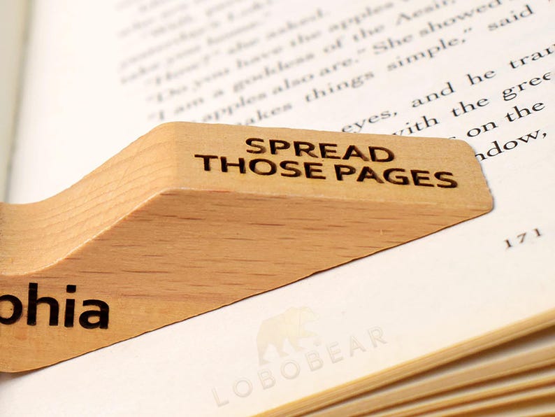 Peut inclure: Un serre-livres en bois avec le texte "SPREAD THOSE PAGES" et le nom "Sophia" grav&eacute; dessus. Le serre-livres est pos&eacute; sur un livre avec le texte "LOBOBEAR" imprim&eacute; sur la page.