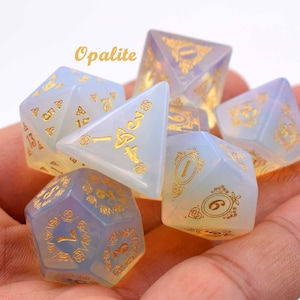 May include: Set of six iridescent opalescent dice with gold metallic numbers and symbols. The dice are in a hand, ready to be rolled.