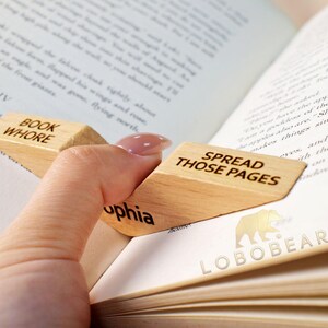 Peut inclure: Deux serre-livres en bois avec le texte "Book Whore" et "Spread Those Pages" dessus. Les serre-livres ont la forme d'un coin et sont utilis&eacute;s pour maintenir un livre ouvert.
