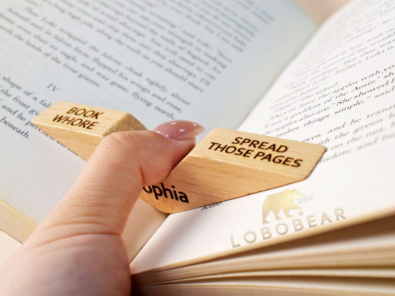 Peut inclure: Deux serre-livres en bois avec le texte "Book Whore" et "Spread Those Pages" dessus. Les serre-livres ont la forme d'un coin et sont utilis&eacute;s pour maintenir un livre ouvert.