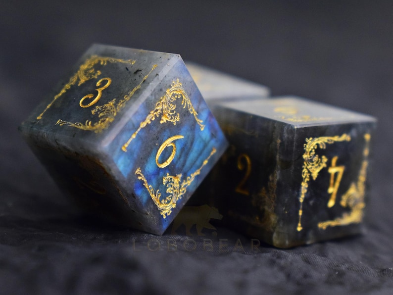 Peut inclure: Gros plan sur trois d&eacute;s &agrave; l'aspect sombre et marbr&eacute;. Les d&eacute;s ont des chiffres dor&eacute;s et des motifs de filigrane dor&eacute;s orn&eacute;s sur chaque face. Les chiffres 3, 6, 2 et 7 sont visibles. Les d&eacute;s sont pour les jeux de soci&eacute;t&eacute;.