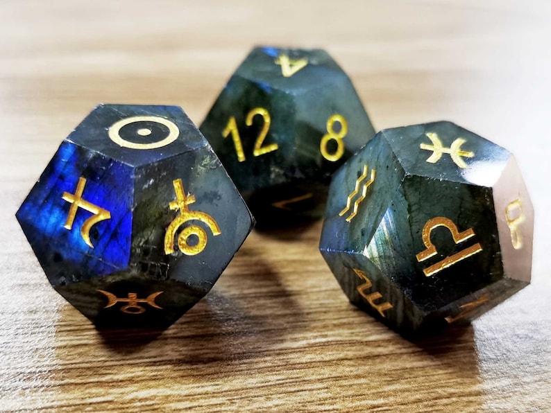 May include: Three dark blue and green gemstone dice with gold zodiac symbols. The dice are shaped like a dodecahedron and have the numbers 12 and 8 on one die.