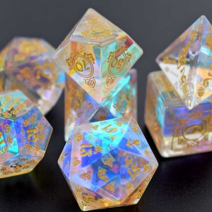May include: Set of iridescent dice with gold numbers and intricate designs. The dice are made of clear resin with a rainbow effect.