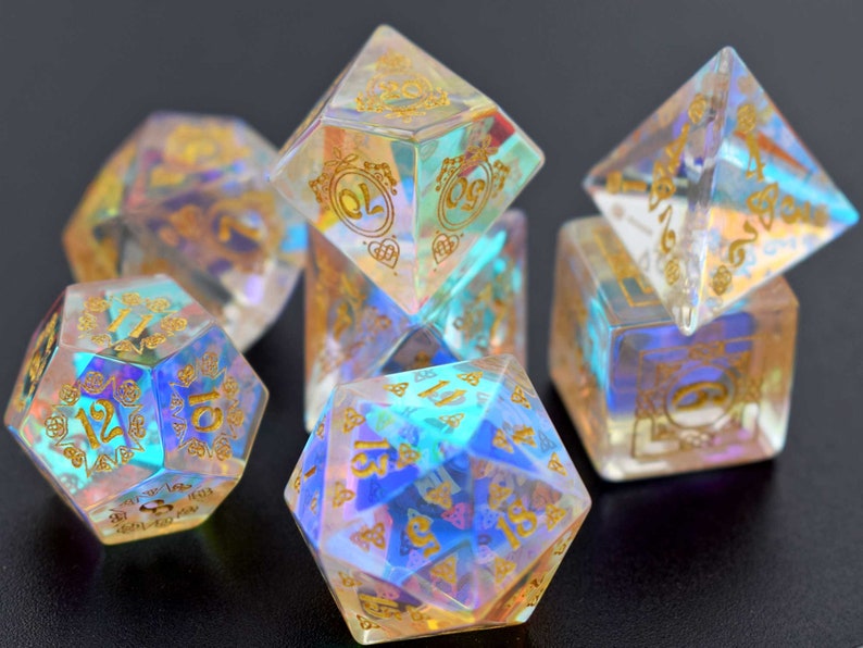 May include: Set of iridescent dice with gold numbers and intricate designs. The dice are made of clear resin with a rainbow effect.