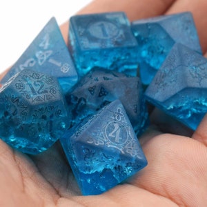 May include: A set of six blue dice with intricate designs and numbers etched into the surface. The dice are made of a translucent material, giving them a frosted appearance.