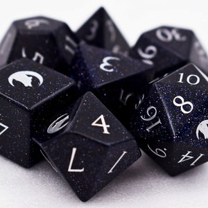 Puede incluir: Un conjunto de dados poli&eacute;dricos en varias formas, incluyendo un d4, d6, d8, d10, d12 y d20. Los dados son de color azul oscuro con un aspecto moteado y brillante y numeraci&oacute;n blanca. Cada dado presenta un s&iacute;mbolo blanco.