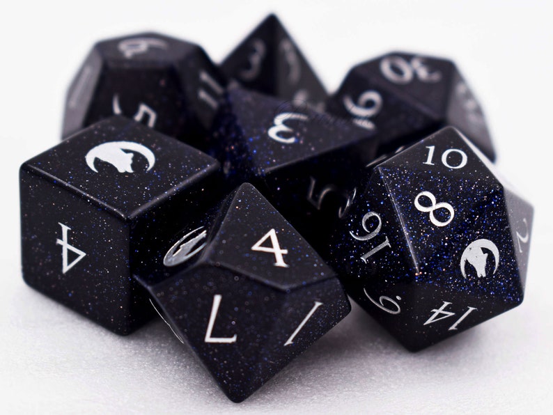 Puede incluir: Un conjunto de dados poli&eacute;dricos en varias formas, incluyendo un d4, d6, d8, d10, d12 y d20. Los dados son de color azul oscuro con un aspecto moteado y brillante y numeraci&oacute;n blanca. Cada dado presenta un s&iacute;mbolo blanco.