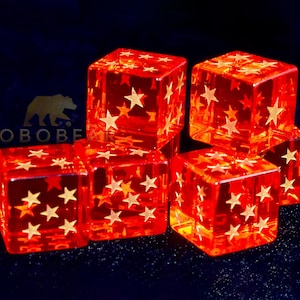 Puede incluir: Seis dados rojos translúcidos con patrones de estrellas doradas apilados sobre un fondo azul oscuro. Los dados están iluminados, creando un efecto brillante. El logotipo "LOBEBEAR" es visible en la esquina superior izquierda.
