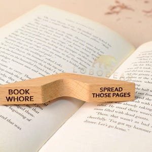 Peut inclure: Un serre-livres en bois avec une forme incurv&eacute;e. Le c&ocirc;t&eacute; gauche dit "Book Whore" et le c&ocirc;t&eacute; droit dit "Spread Those Pages".