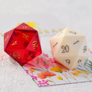 May include: Two twenty-sided dice, one red and one white, with gold numbers. The dice are on a floral card.