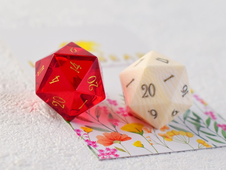 May include: Two twenty-sided dice, one red and one white, with gold numbers. The dice are on a floral card.