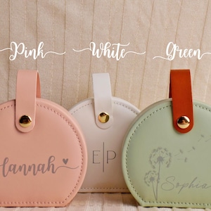 K&ouml;nnte beinhalten: Drei runde, pastellfarbene Etuis mit Griffen. Das rosa Etui tr&auml;gt den Namen "Hannah". Das wei&szlig;e Etui hat die Initialen "EP". Das gr&uuml;ne Etui hat ein Pusteblumen-Design und den Namen "Sophia". Jedes Etui hat einen goldenen Knopf.