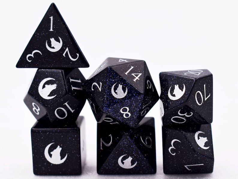 Puede incluir: Un juego de siete dados poli&eacute;dricos en un dise&ntilde;o azul oscuro moteado. Cada dado presenta n&uacute;meros blancos y un s&iacute;mbolo blanco de lobo y luna creciente. Los dados son para juegos de mesa.