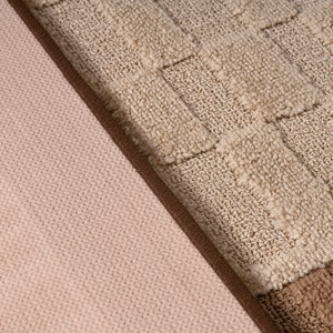 Pode incluir: Close-up de dois tecidos com texturas diferentes. Um &eacute; um tecido rosa claro com um padr&atilde;o tecido sutil. O outro &eacute; um tecido bege com um padr&atilde;o quadriculado em relevo.