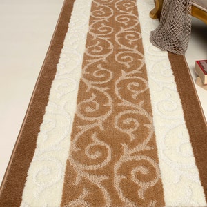 May include: A brown and white patterned runner rug with a floral design. The rug has a brown border and a white center with a brown floral pattern.