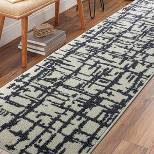 May include: A black and white geometric patterned runner rug with a modern design. The rug is placed on a hardwood floor.