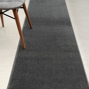 May include: A dark gray runner rug with a smooth texture. The rug is placed on a white floor.