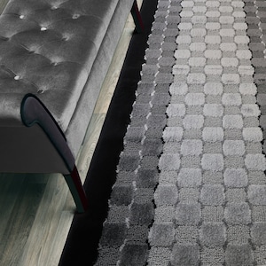 May include: A gray and black patterned rug with a geometric design. The rug has a black border and is made of a soft, plush material.