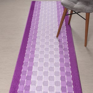 May include: A long, rectangular purple and white checkered runner rug. The rug has a gradient of purple shades, with the darkest purple at the edges and the lightest purple in the center. The rug is made of a soft, plush material.